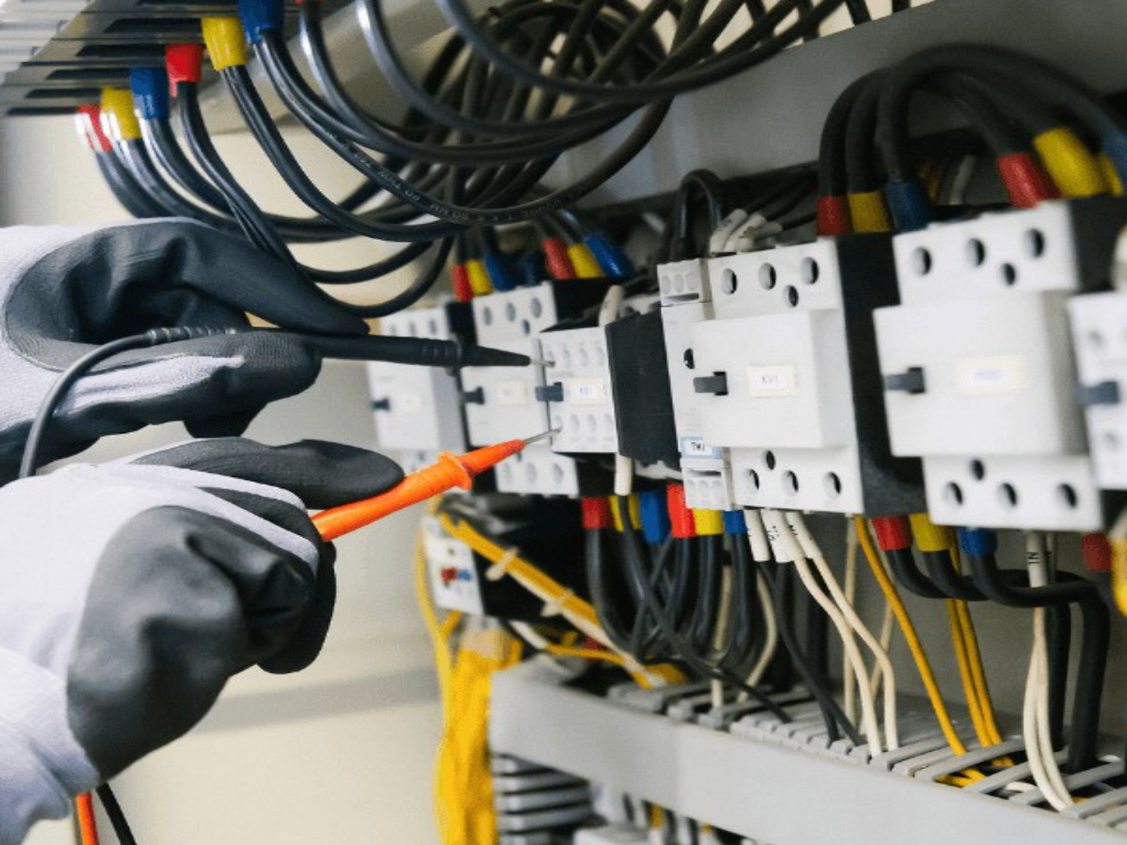 An electrician's gloved hands working inside an open electrical panel
